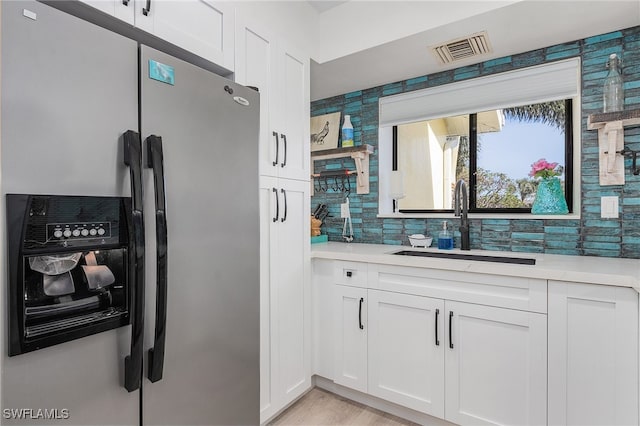 kitchen featuring white cabinetry, sink, stainless steel fridge with ice dispenser, backsplash, and light hardwood / wood-style floors