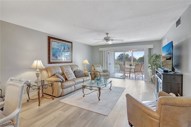 living room with a textured ceiling, light wood-type flooring, and ceiling fan