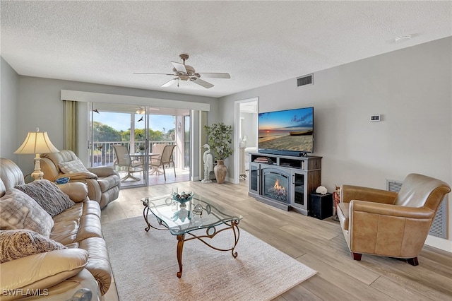 living room with ceiling fan, a textured ceiling, and light wood-type flooring