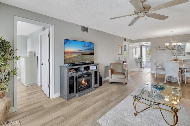 living room featuring ceiling fan with notable chandelier, a textured ceiling, and light hardwood / wood-style floors