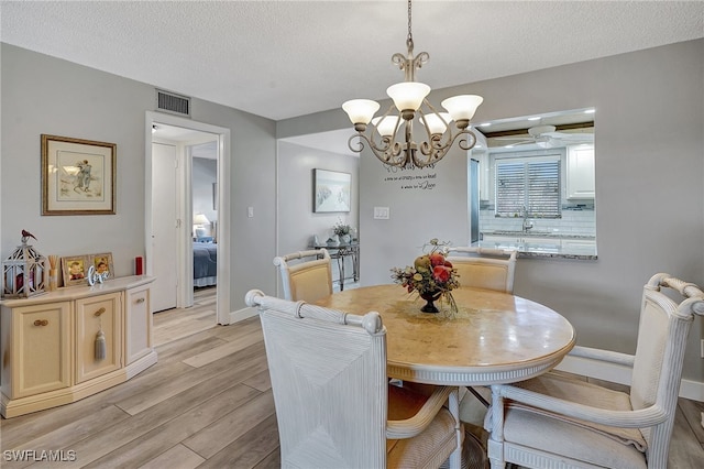 dining room featuring sink, an inviting chandelier, a textured ceiling, and light wood-type flooring