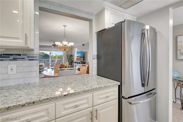 kitchen featuring stainless steel fridge, an inviting chandelier, backsplash, light stone countertops, and white cabinets