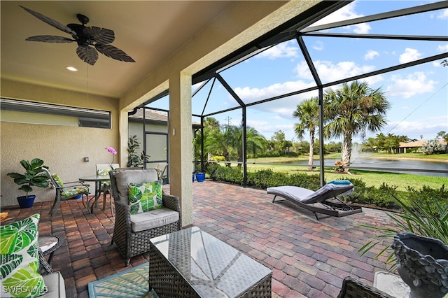 view of patio featuring a water view, glass enclosure, and ceiling fan