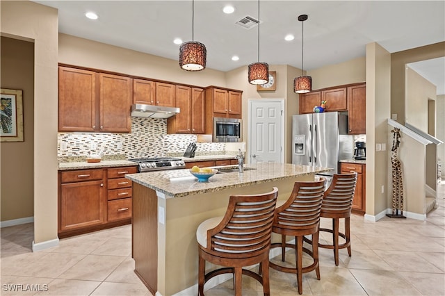 kitchen featuring light stone countertops, a kitchen breakfast bar, stainless steel appliances, a kitchen island with sink, and hanging light fixtures