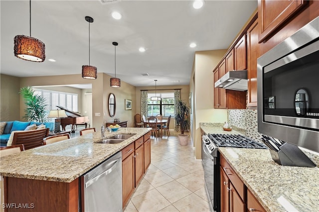 kitchen featuring light stone countertops, stainless steel appliances, hanging light fixtures, and an island with sink