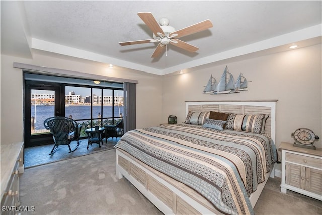 bedroom featuring ceiling fan, carpet floors, a tray ceiling, access to exterior, and a water view