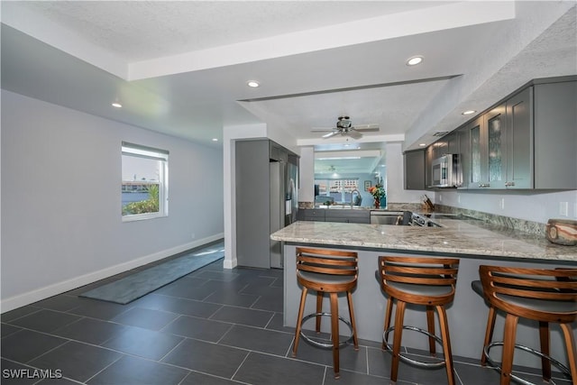 kitchen with ceiling fan, stainless steel appliances, kitchen peninsula, and a tray ceiling