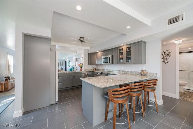 kitchen featuring kitchen peninsula, gray cabinets, ceiling fan, stainless steel appliances, and a kitchen breakfast bar