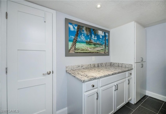 bar featuring white cabinets, light stone countertops, dark tile patterned flooring, and a textured ceiling