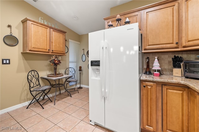 kitchen featuring light stone countertops, backsplash, vaulted ceiling, white fridge with ice dispenser, and light tile patterned flooring