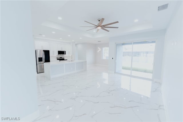 unfurnished living room featuring a raised ceiling, ceiling fan, and sink