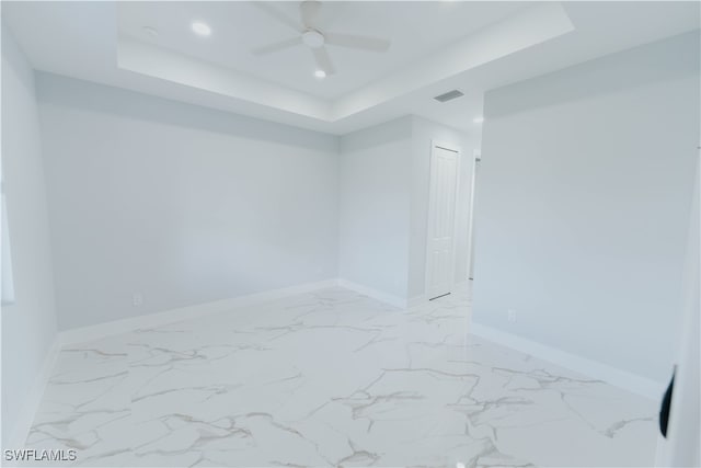 empty room with ceiling fan and a raised ceiling