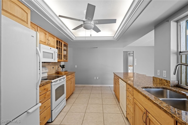 kitchen with ceiling fan, sink, a raised ceiling, dark stone counters, and white appliances