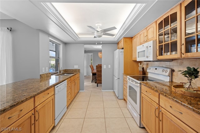 kitchen featuring backsplash, dark stone counters, white appliances, a tray ceiling, and light tile patterned floors