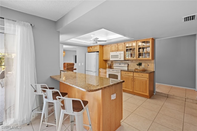 kitchen featuring a kitchen bar, white appliances, kitchen peninsula, and dark stone counters