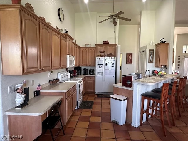 kitchen with white appliances, dark tile patterned flooring, a kitchen breakfast bar, ceiling fan, and a towering ceiling