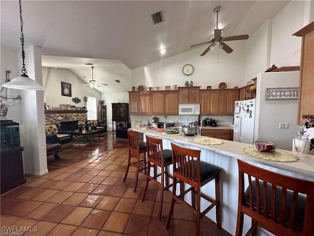 kitchen with a kitchen breakfast bar, white appliances, dark tile patterned floors, decorative light fixtures, and high vaulted ceiling