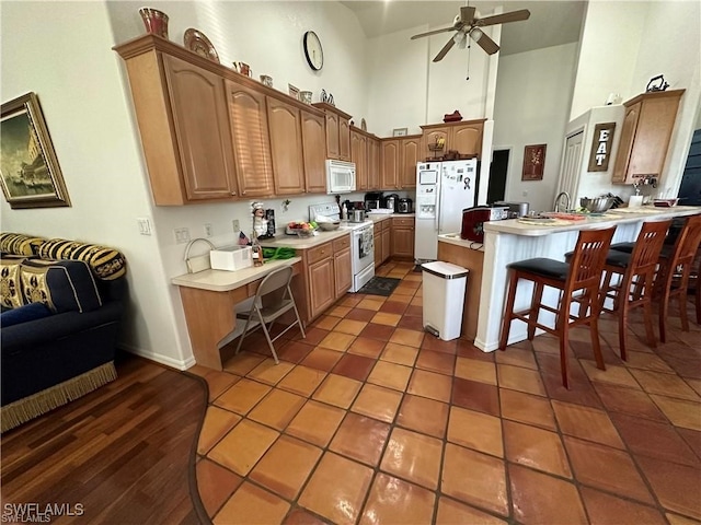 kitchen with a kitchen bar, kitchen peninsula, a towering ceiling, white appliances, and dark hardwood / wood-style floors