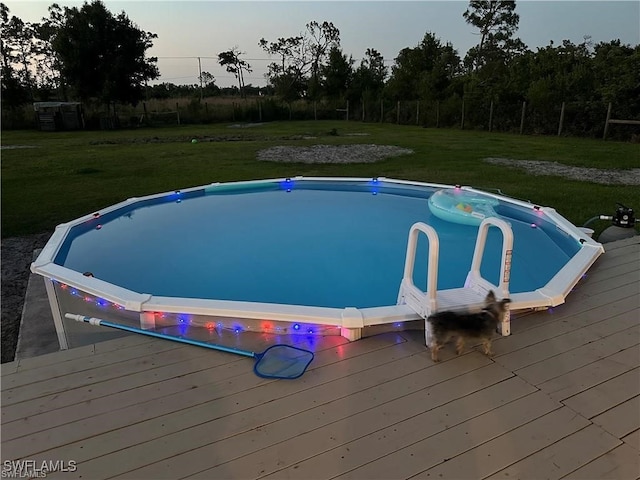 pool at dusk with a yard and a deck