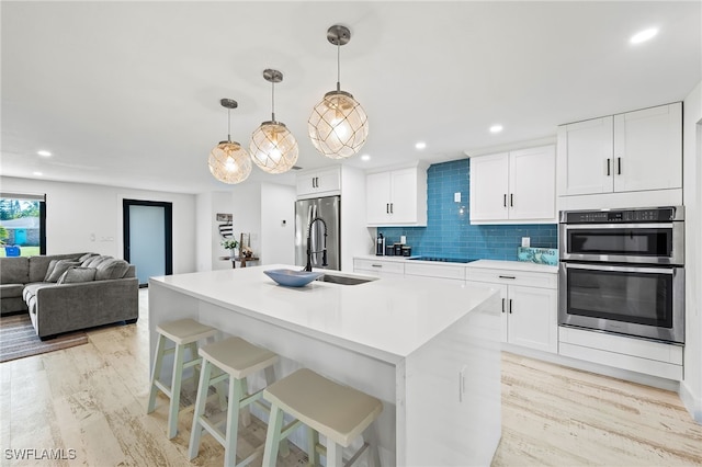 kitchen featuring decorative light fixtures, white cabinetry, a center island with sink, and light hardwood / wood-style flooring