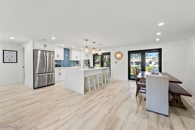 kitchen with white cabinetry, light countertops, light wood-type flooring, stainless steel refrigerator, and tasteful backsplash