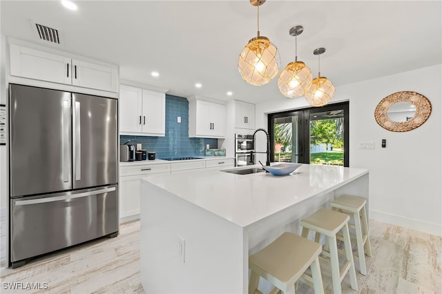 kitchen featuring stainless steel appliances, an island with sink, light hardwood / wood-style floors, decorative light fixtures, and white cabinets