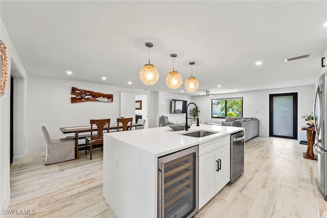 kitchen with beverage cooler, open floor plan, decorative light fixtures, light wood-style floors, and a sink