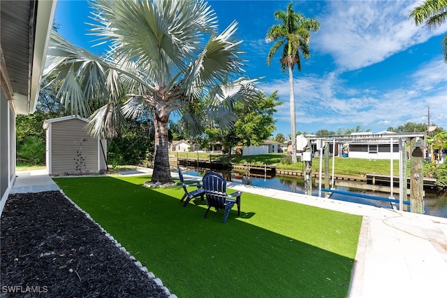 view of yard featuring boat lift, a water view, a storage shed, a boat dock, and an outdoor structure