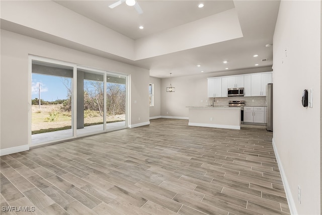 unfurnished living room with ceiling fan, light wood-style flooring, recessed lighting, a sink, and baseboards