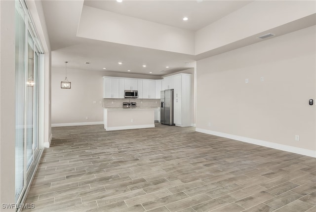 kitchen with stainless steel appliances, light wood-type flooring, open floor plan, and backsplash