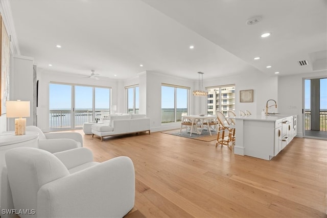 living room featuring sink, light wood-type flooring, a water view, ceiling fan with notable chandelier, and ornamental molding