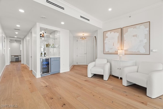 sitting room with light hardwood / wood-style floors, crown molding, wine cooler, and bar area