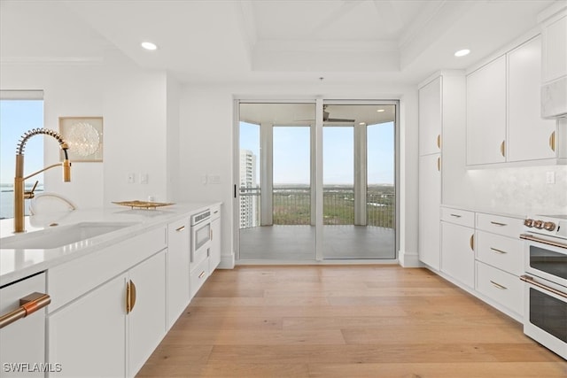 kitchen featuring stove, light wood-type flooring, crown molding, sink, and white cabinetry