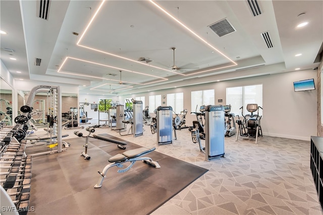 workout area featuring a raised ceiling, ceiling fan, and light carpet