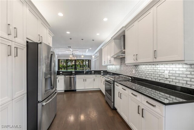 kitchen featuring stainless steel appliances, wall chimney range hood, dark hardwood / wood-style floors, dark stone countertops, and white cabinets