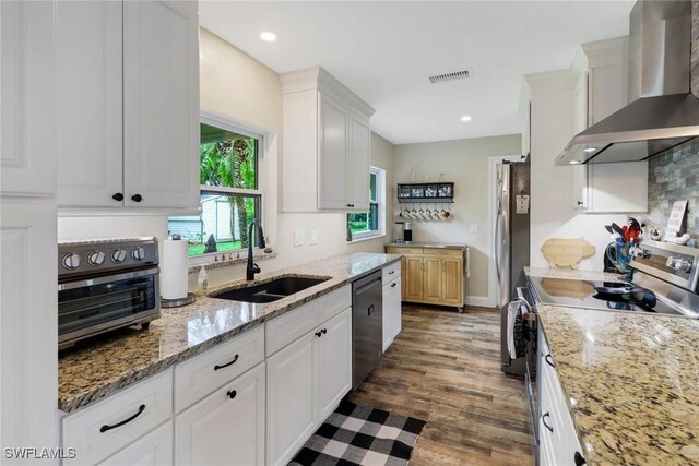 kitchen featuring sink, wall chimney exhaust hood, appliances with stainless steel finishes, light stone counters, and white cabinetry