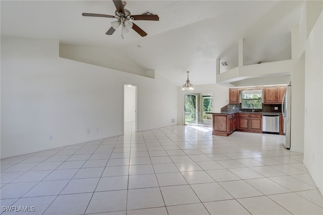 unfurnished living room with ceiling fan with notable chandelier, light tile patterned floors, sink, and high vaulted ceiling