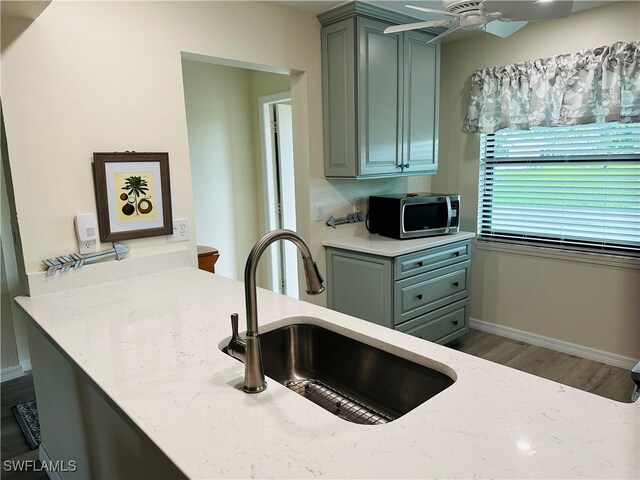 kitchen with light stone counters, ceiling fan, sink, and hardwood / wood-style floors