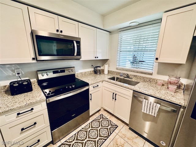 kitchen featuring white cabinets, appliances with stainless steel finishes, light stone countertops, and sink