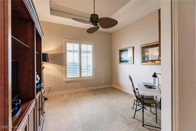 carpeted office space featuring ceiling fan and a tray ceiling