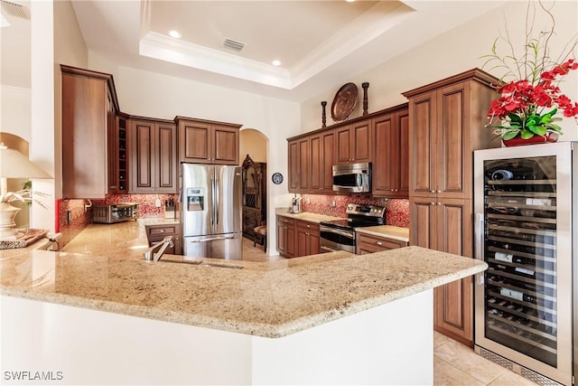 kitchen with appliances with stainless steel finishes, kitchen peninsula, beverage cooler, decorative backsplash, and a tray ceiling