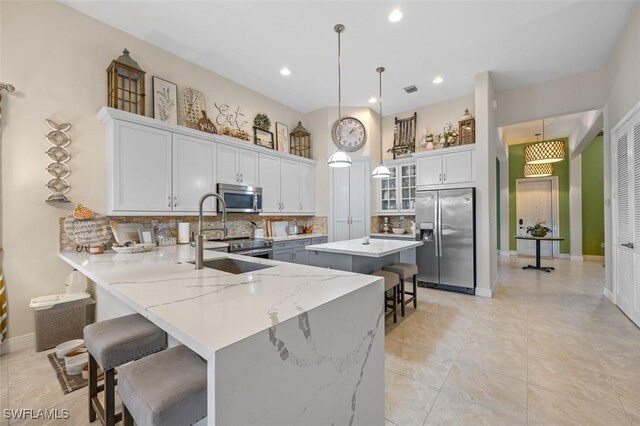 kitchen featuring backsplash, appliances with stainless steel finishes, decorative light fixtures, kitchen peninsula, and a breakfast bar area