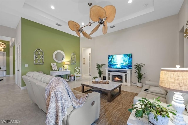 living room with recessed lighting, visible vents, a ceiling fan, a lit fireplace, and a tray ceiling