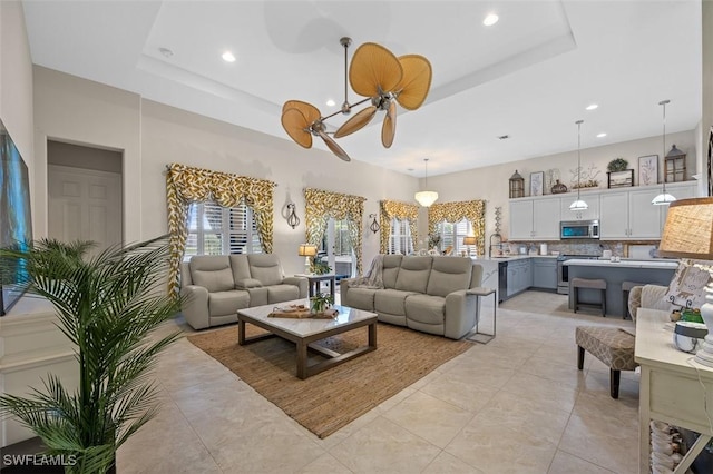 living room featuring light tile patterned floors, a tray ceiling, ceiling fan, and sink