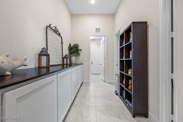 hall with light tile patterned floors, visible vents, and baseboards