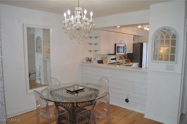 dining area featuring light wood-type flooring, a textured ceiling, and a chandelier