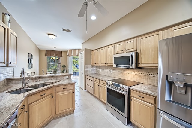 kitchen featuring light stone counters, sink, stainless steel appliances, and decorative light fixtures