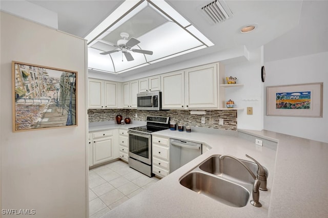 kitchen with appliances with stainless steel finishes, backsplash, sink, light tile patterned floors, and white cabinets