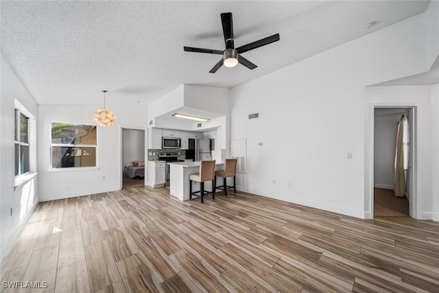 unfurnished living room featuring a textured ceiling, ceiling fan with notable chandelier, light hardwood / wood-style floors, and vaulted ceiling