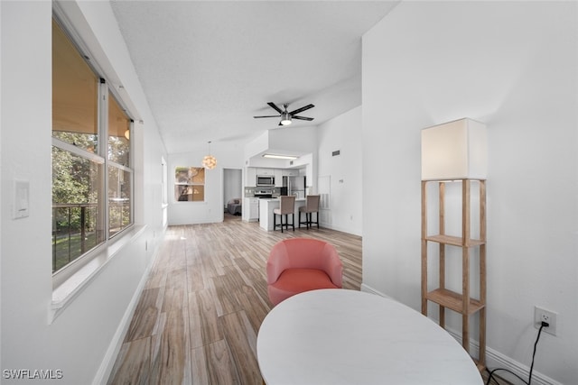 dining room with ceiling fan, light hardwood / wood-style flooring, and vaulted ceiling